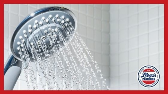 A round chrome showerhead emitting water in a white tile bathroom