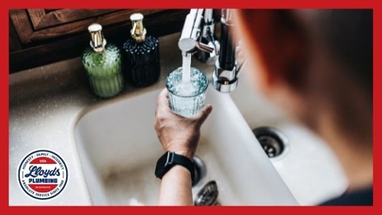 A person holding a glass of water under a running sink