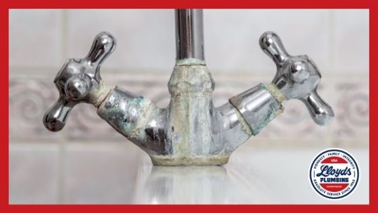 A silver faucet with two handles covered in green and white limescale.